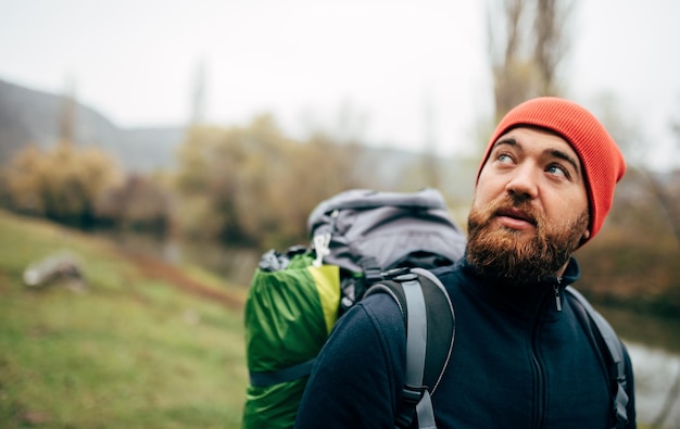 Close up horizontal outdoor portrait of hiker young male hiking in mountains with travel backpack Traveler man with beard trekking and mountaineering Travel people healthy lifestyle concept