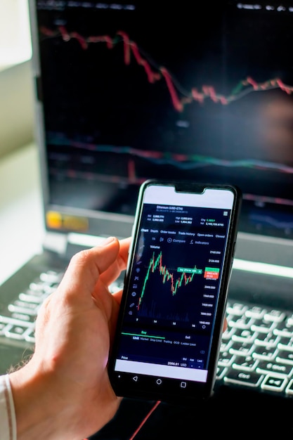 Close-up of human hand holding mobile phone with financial graph. Online trading crypto currency