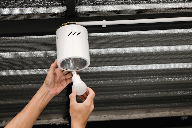 Close up human hand is installing an LED light bulb in a circular ceiling lamp