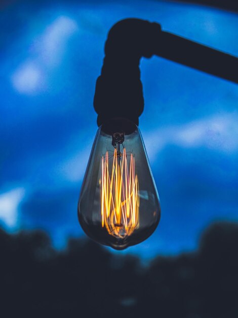 Close-up of illuminated light bulb against blue sky