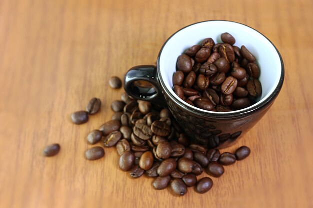 close-up image of dark roasted coffee beans in ceramic espresso cup on wooden background