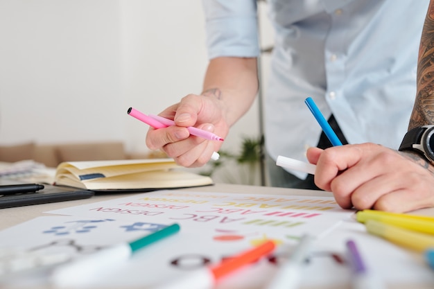 Close-up image of graphic designer drawing sketches of company logo with colorful felt-tip pens