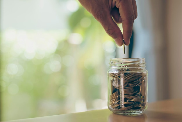 Close up image hand of businessman holding coins putting in glass concept saving money for finance accounting education and investment