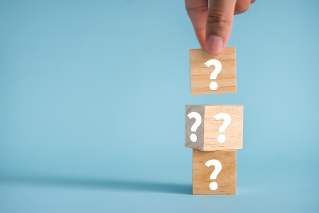 Close up image of hand was holding wooden cube block shape with sign question mark symbol on blue background It is an image that conveys different questions