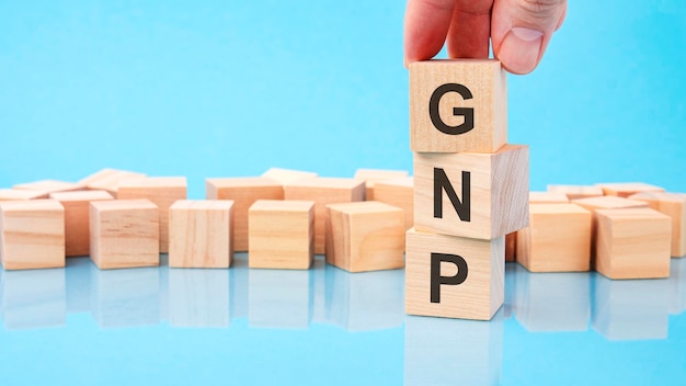 Close up image hand of a young businessman holding a wooden cube with letter G GNP on wooden cube on a blue background with copy space