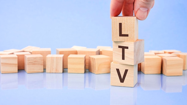 Close up image hand of a young businessman holding a wooden cube with letter L LTV on wooden cube on a blue background with copy space