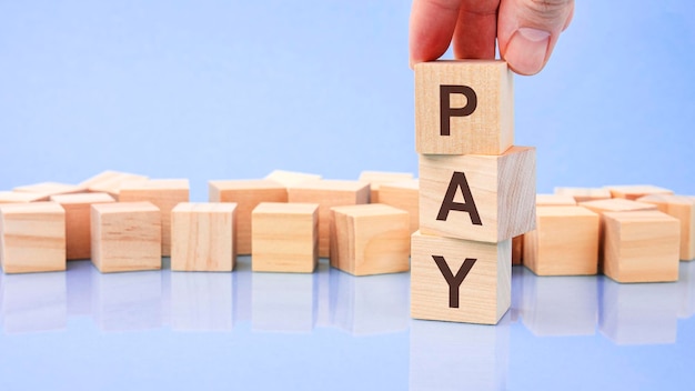 Close up image hand of a young businessman holding a wooden cube with letter P PAY on wooden cube on a blue background with copy space