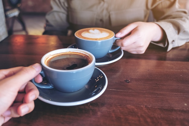 Close up image of a man and a woman clinking blue coffee mugs on wooden table in cafe