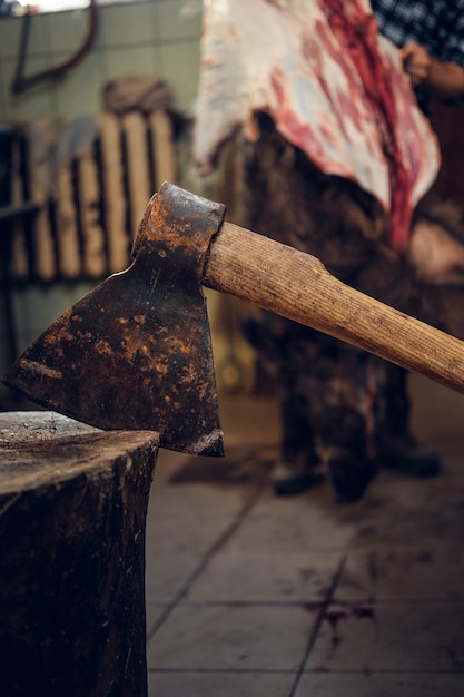 Close up image of meat axe over bearded butcher cuts up the carcass of wild pig on background.