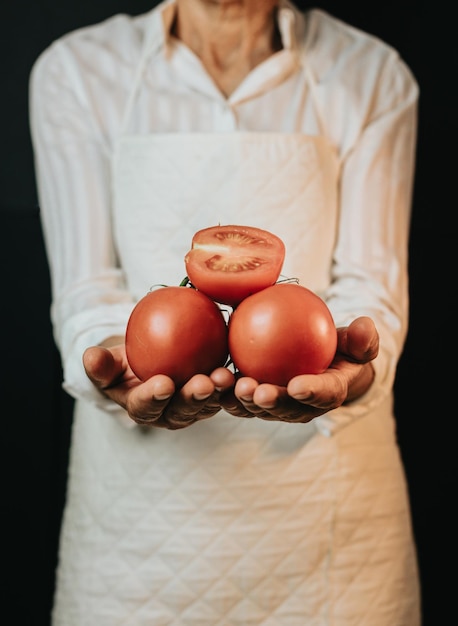 Close up image of an old woman cooking chef grabbing fresh tomatoes showing to camera before preparing them in a healthy foodRustic cuisine cooking made by chef Preparing ingredient for a bio meal