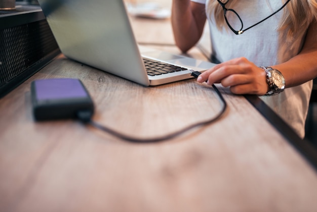 Close-up image of a woman freelancer connecting an external hard drive to the laptop.