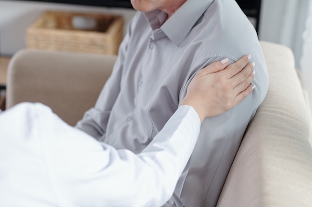 Close-up image of woman touching shoulder of senior patient when trying to support him