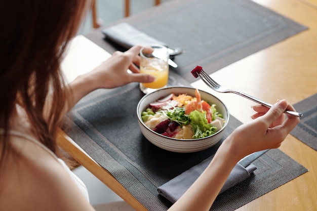 Photo close-up image of young woman eating poke bowl with shrimps for lunch at cafe table