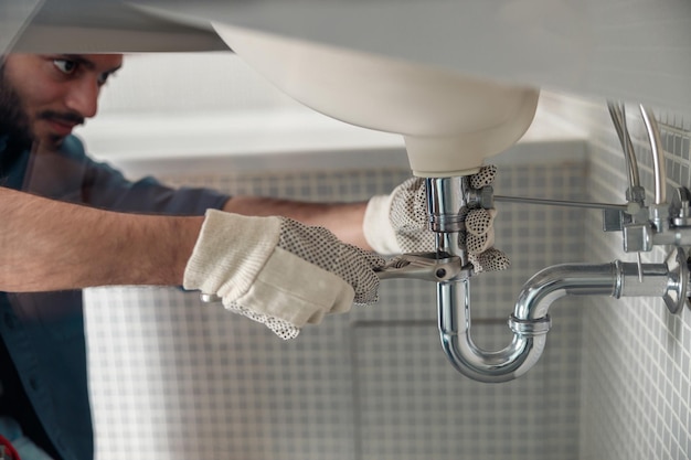 Photo close up of indian plumber is repairing faucet of a sink at bathroom using adjustable wrench