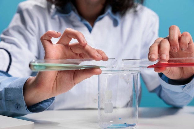 Close up of insane maniac chemist mixing toxic unidentified compounds using glass tubes and beaker while sitting at desk in laboratory. Crazy foolish biochemist with beakers experimenting new formula.