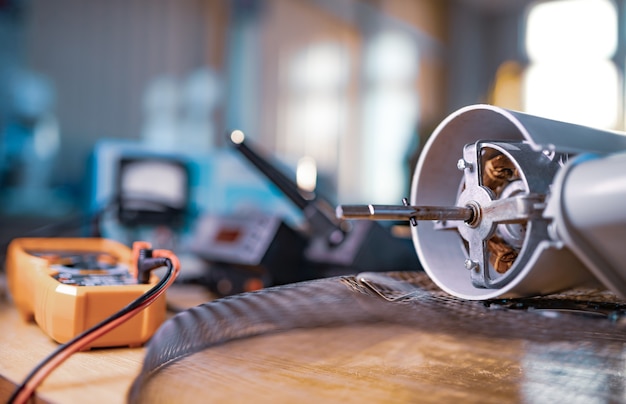 Close-up of an iron motor from home cooling fan and testind tools lies on a table in workshop. The concept of repair and restoration of damaged equipment