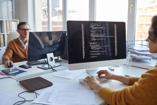 Close up of IT developer writing code on computer screen while collaborating on project with team of software designers, copy space