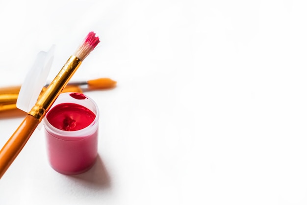 Close up of jar with red gouache paint and brushes on white paper background