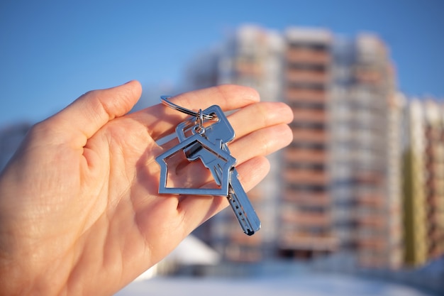 Close-up of key with keychain in shape of house in hand.