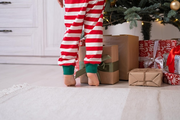 close up kid legs in Christmas pajamas near gift boxes and Christmas tree