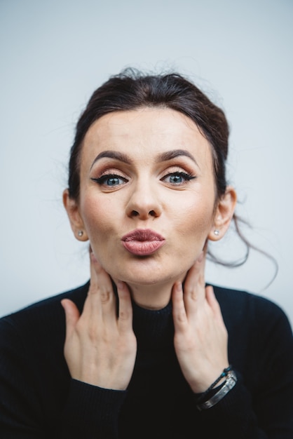 Close-up kiss from a young caucasian brunette woman in black with blue eyes in the studio with white background.