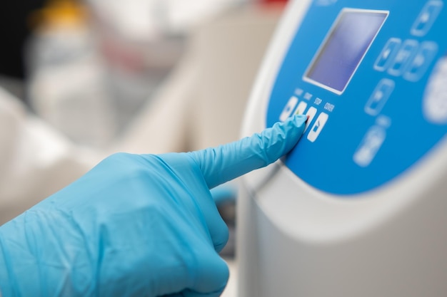 Close up laboratory worker hand in rubber gloves sets parameters on the centrifuge for sample prepar