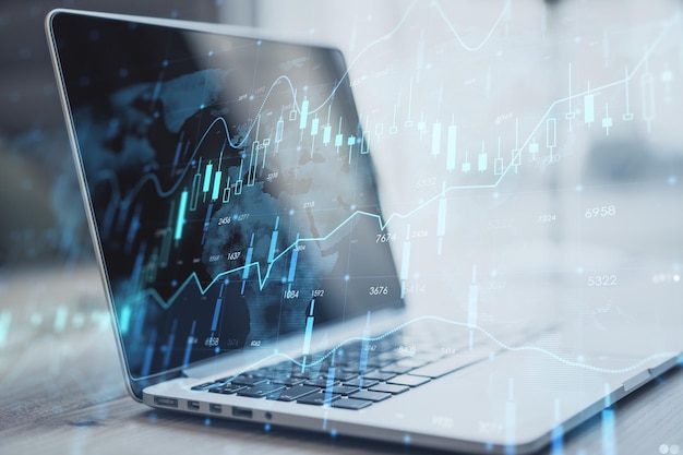 Close up of laptop on desktop with creative glowing forex chart hologram and map on blurry background Stock market and invest concept Double exposure