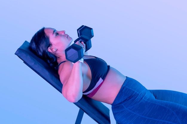 Close up of a latin woman with two dumbbells lying on a bench doing chest press