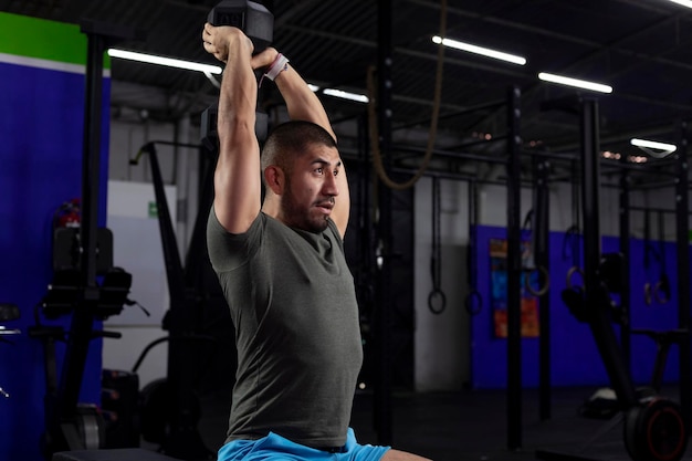 Close up of a latino athlete doing triceps exercise in a gym with a dumbbell