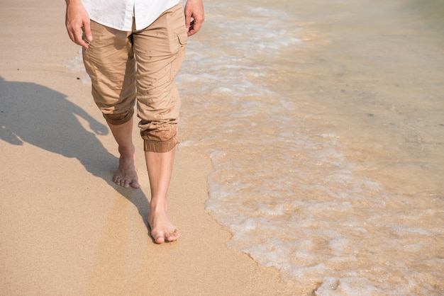 close-up leg of man is standing on the beach with wave from sea in morning at summer