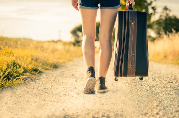 Close up of legs of a woman at vacation walking on the road holding her suitcase on a countryside