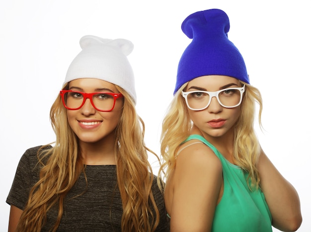 Close up lifestyle portrait of two pretty teen girlfriends smiling and having fun, wearing hipster clothes, hats and glasses, positive mood.