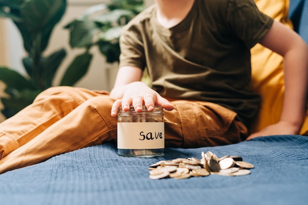 Close up of little child kid boy hands grabbing and putting stack coins in to glass jar with save