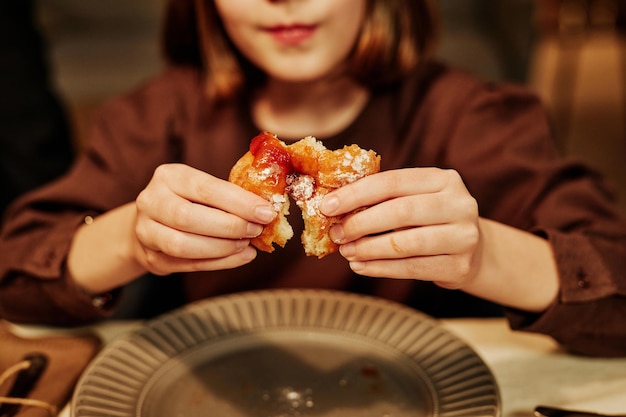 Close up of little girl enjoying homemade pastry with jam at dinner table