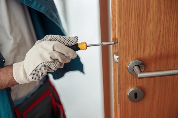 Close up of locksmith workman in uniform installing door knob Professional repair service