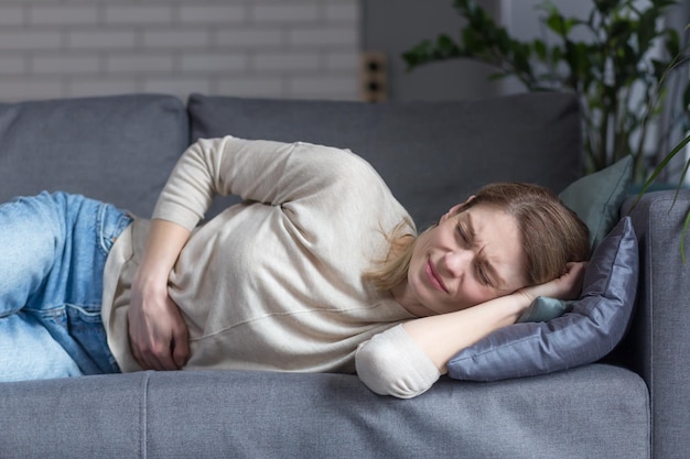 Close up of a lonely woman lying sick on the couch has abdominal pain holding his hand to the side