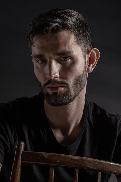 Close up low key portrait of a handsome bearded man sitting on the chair