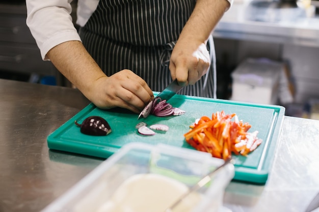 Close up male chef cuts vegetables in restaurant