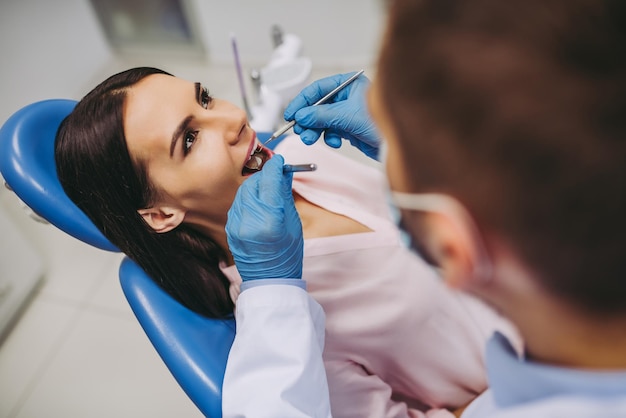 Close up of male dentist checking patient teeth with mirror in modern dental clinic