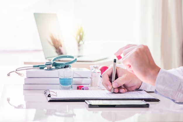 Close-up of a male doctor filling up medical form at clipboard