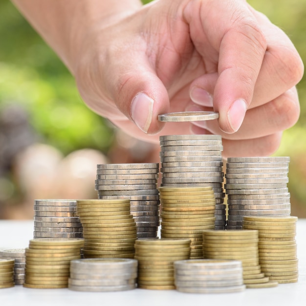 Close up of male hand stacking gold coins with green bokeh background 