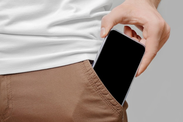 Close up of male hand taking out big mobile phone with empty black screen from front pocket of brown pants on grey background