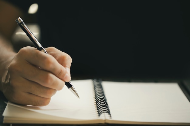 Close up of male hand with pen writing on notebook on wooden table