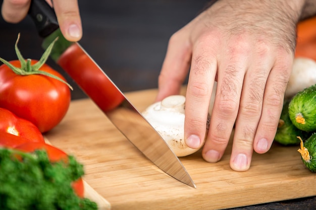 Close up on male hands cutting tomato, making salad. Chief cutting vegetables. Healthy lifestyle, diet food