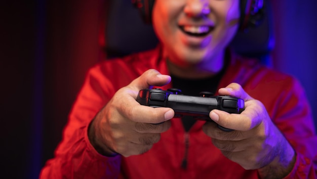 Close up male hands holding joystick game console. Young man playing video game online. Indian man in red jacket play computer pc at home in the dark room