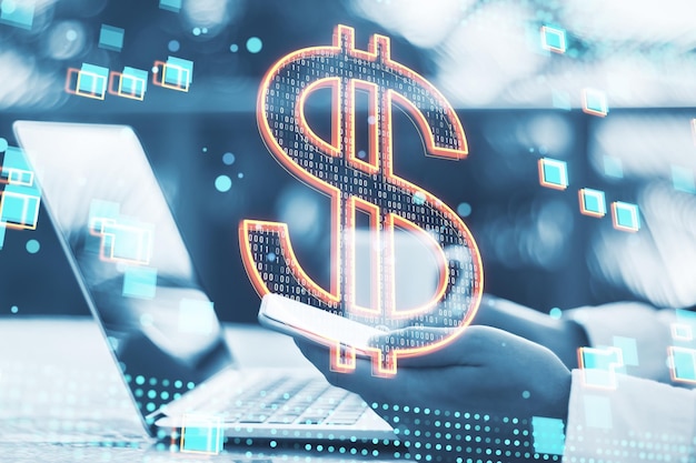 Close up of male hands using laptop and cellphone with glowing dollar sign on blurry desktop and outdoor background Finance trade and money transfer concept Double exposure