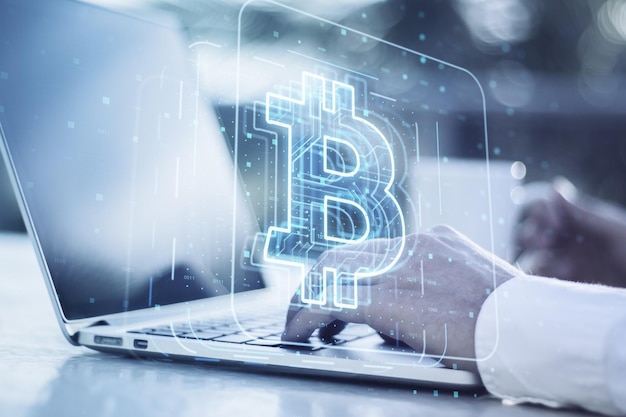 Close up of male hands using laptop computer on desktop with coffee cup and glowing bitcoin hologram on blurry background Mining and trade bitcoin concept Bitcoin hits new record Double exposure