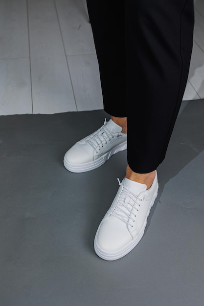 Close up of male legs in black pants and white casual sneakers Men's leather summer shoes