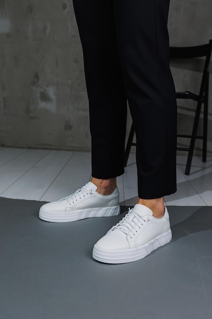 Close up of male legs in black pants and white casual sneakers Men's leather summer shoes