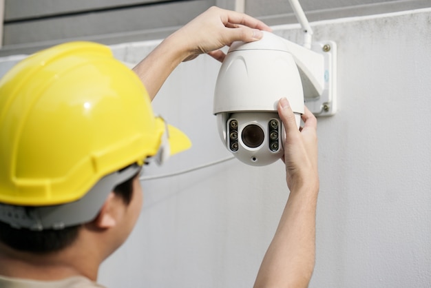 Close Up Of Male Technician Fixing CCTV Camera On Wall